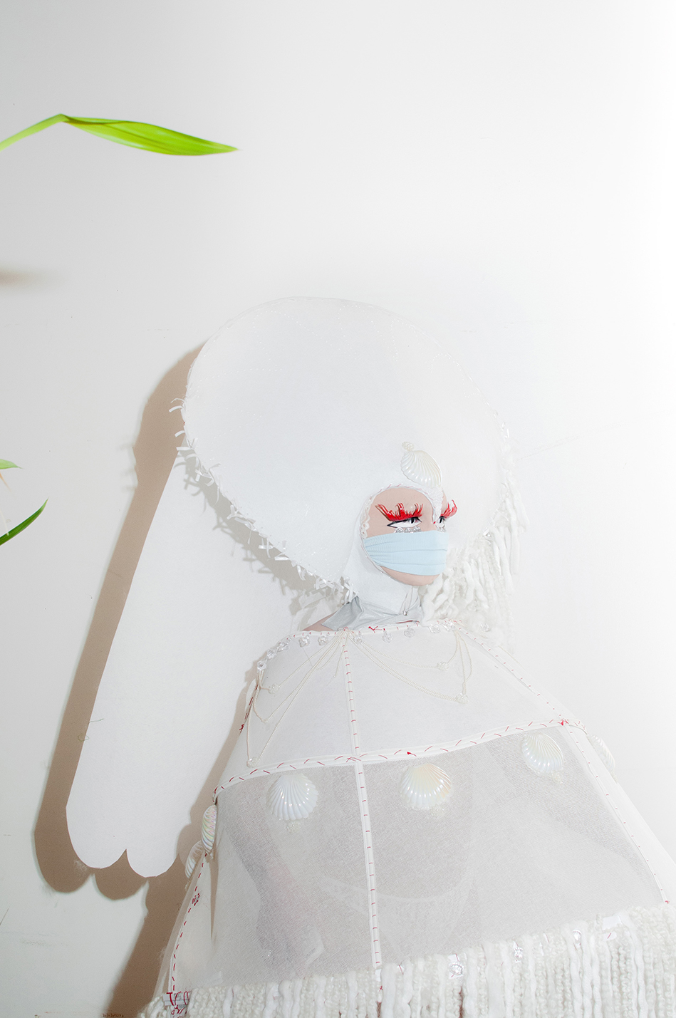 Portrait shot of Bon Bon in a large abstract white ourfit against a white wall
